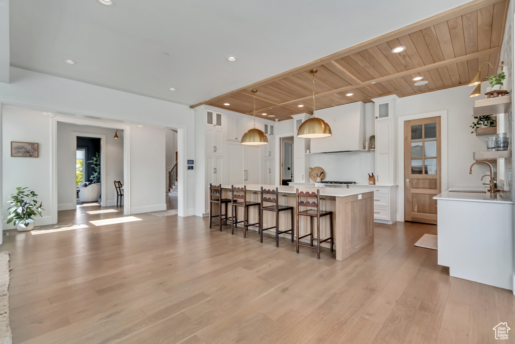 Kitchen featuring a sink, a large island, light countertops, white cabinetry, and wood ceiling