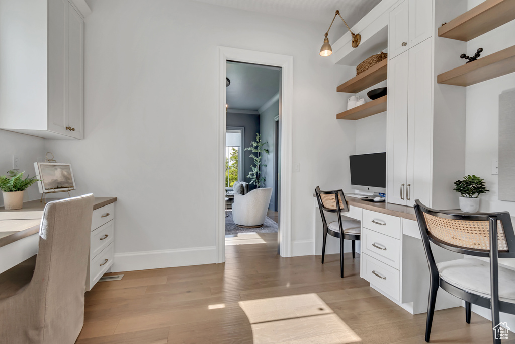 Office area featuring built in study area, light wood-style flooring, baseboards, and crown molding