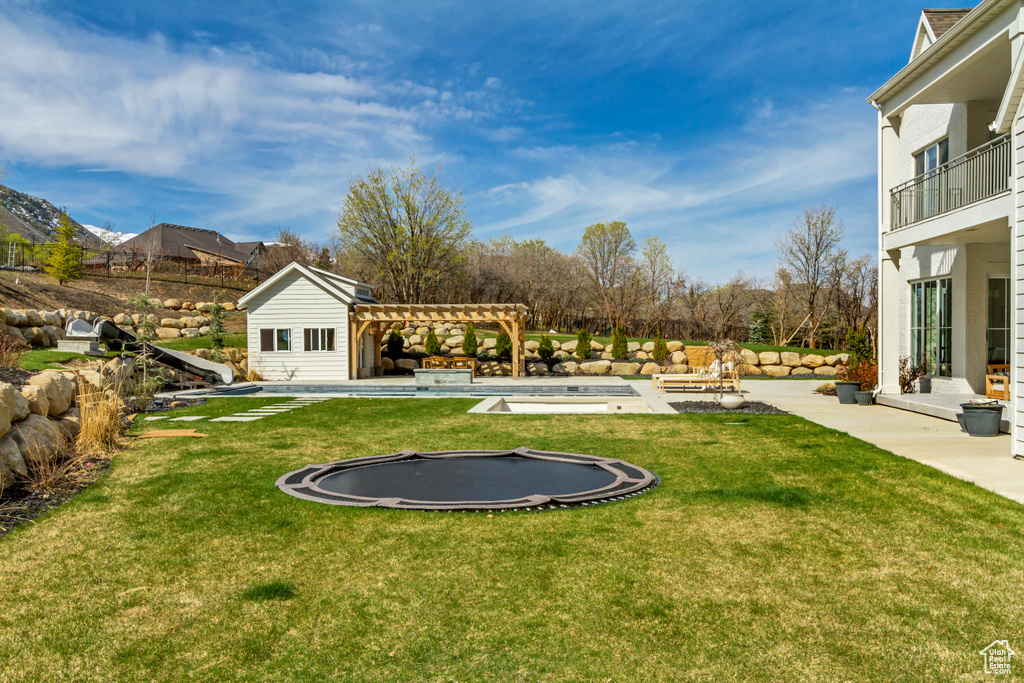 View of grassy yard with a pergola, a trampoline, and a patio