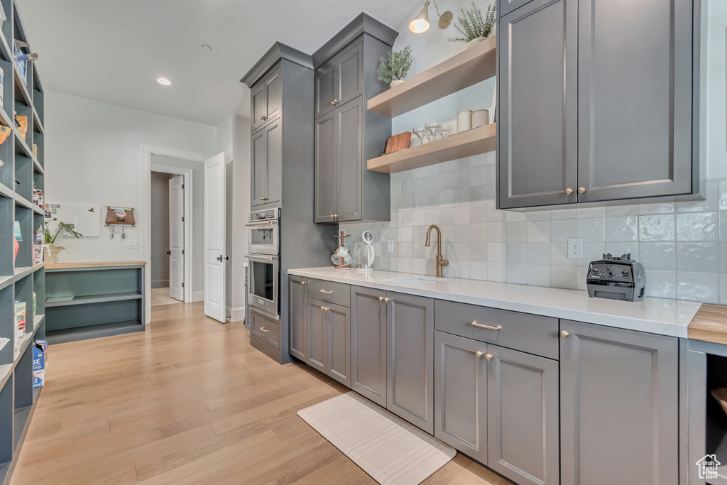 Kitchen with open shelves, gray cabinetry, tasteful backsplash, stainless steel double oven, and light countertops