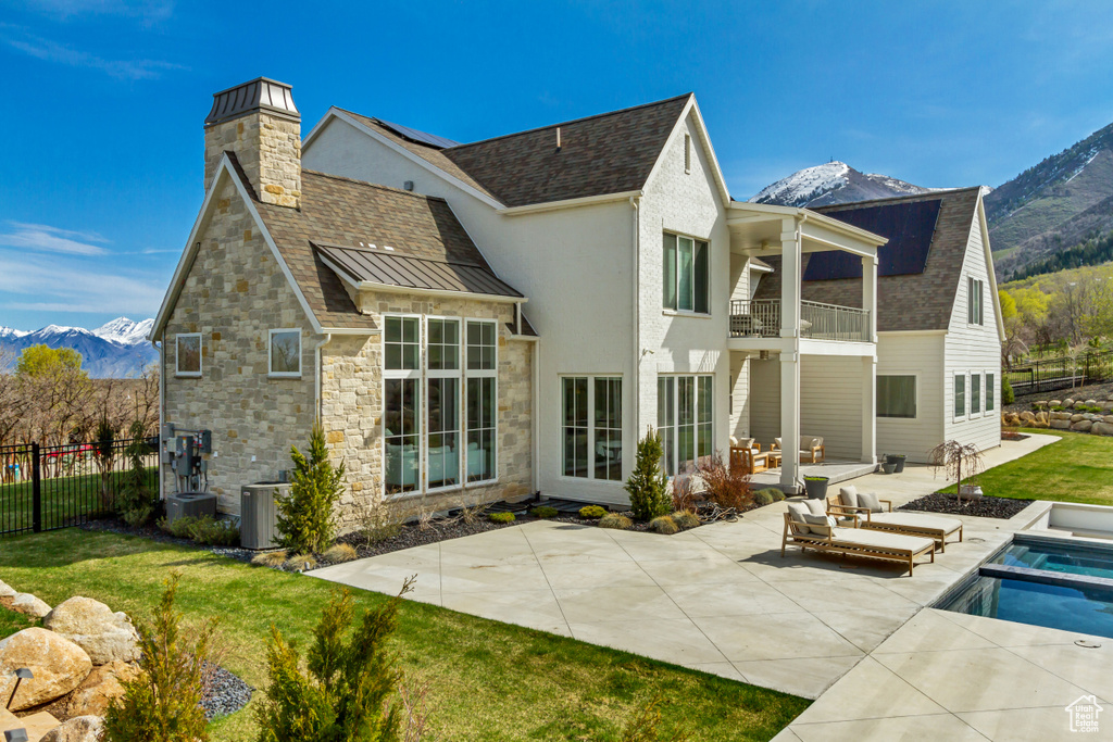 Rear view of house with a balcony, a mountain view, a patio area, a standing seam roof, and stone siding