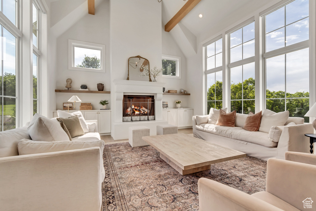 Living area featuring beamed ceiling, high vaulted ceiling, a warm lit fireplace, wood finished floors, and recessed lighting