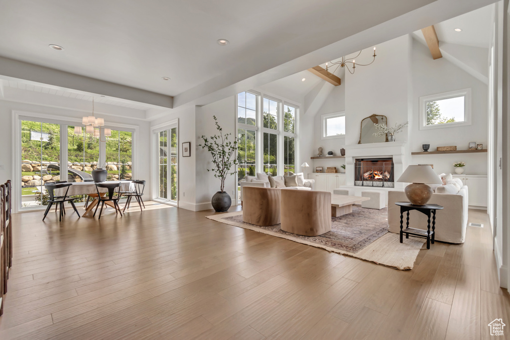 Living room with a chandelier, beam ceiling, wood finished floors, a glass covered fireplace, and plenty of natural light