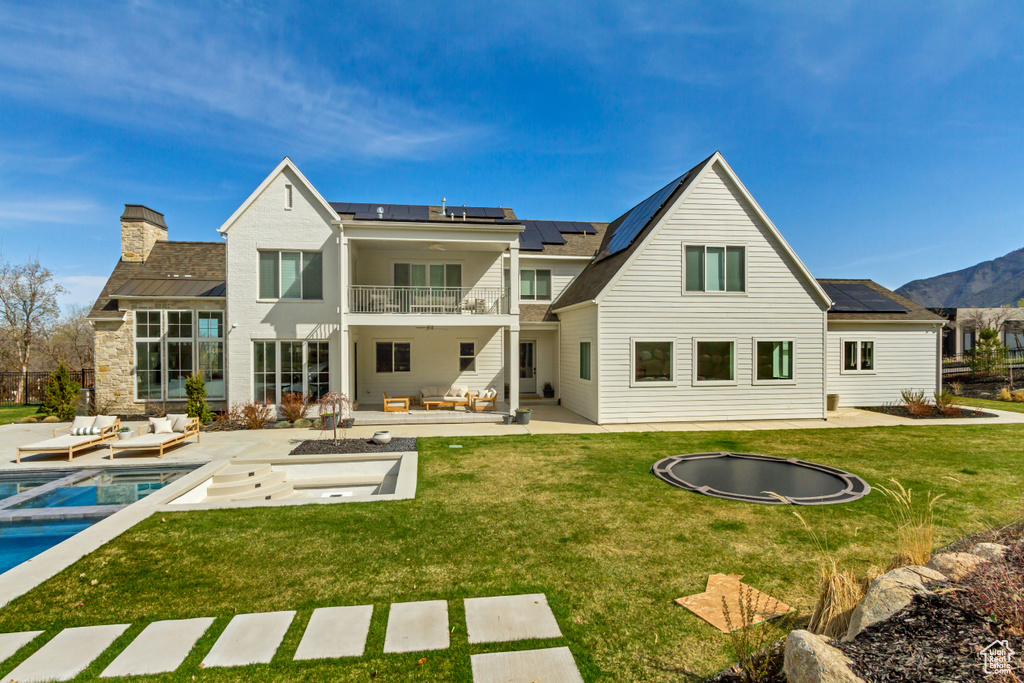 Rear view of property featuring an outdoor living space, a balcony, roof mounted solar panels, and a patio area