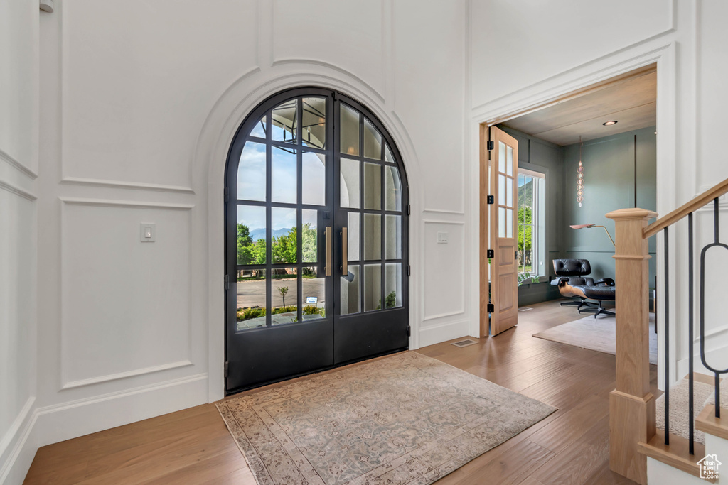 Foyer entrance with a decorative wall, wood finished floors, stairway, a high ceiling, and french doors