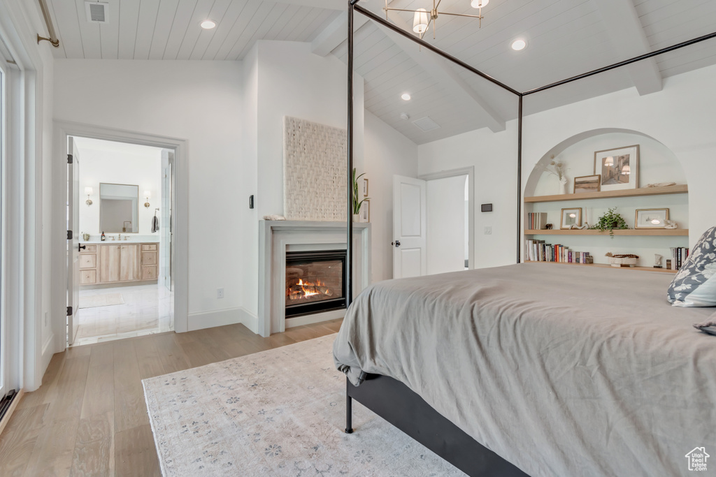 Bedroom with light wood-style floors, a glass covered fireplace, recessed lighting, wooden ceiling, and connected bathroom