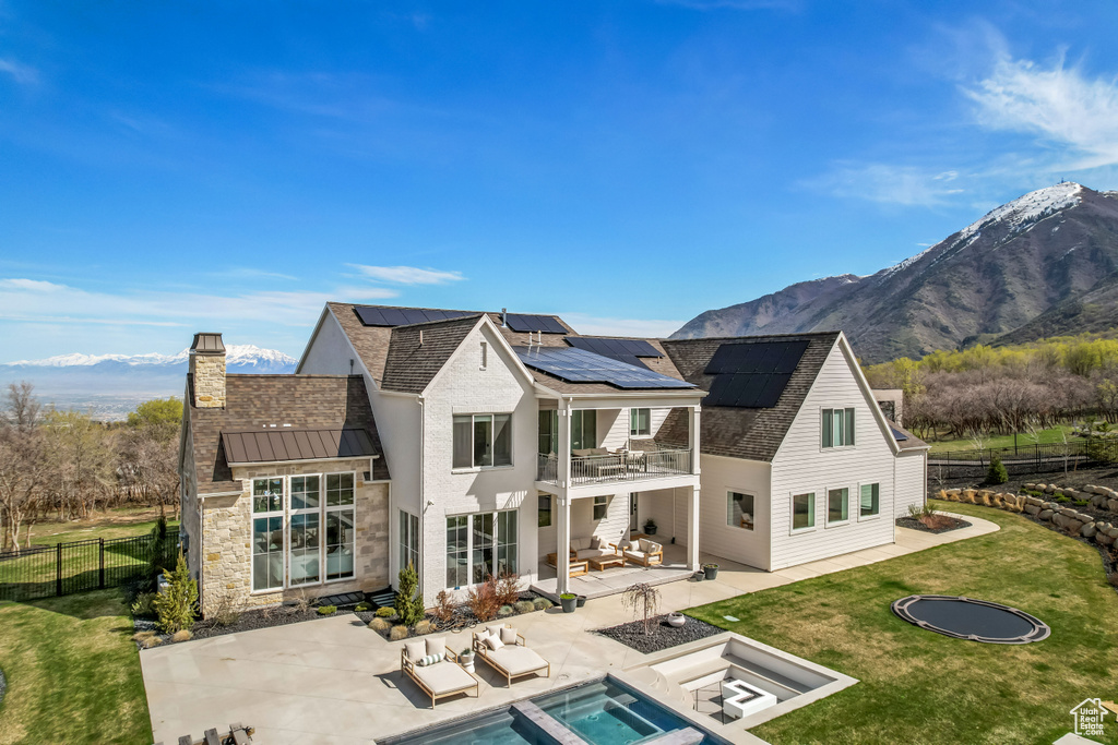 Back of property with an outdoor living space with a fire pit, a balcony, a patio area, roof mounted solar panels, and a standing seam roof