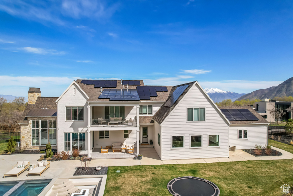 Back of property featuring a balcony, a patio, an outdoor living space with a fire pit, roof mounted solar panels, and a mountain view
