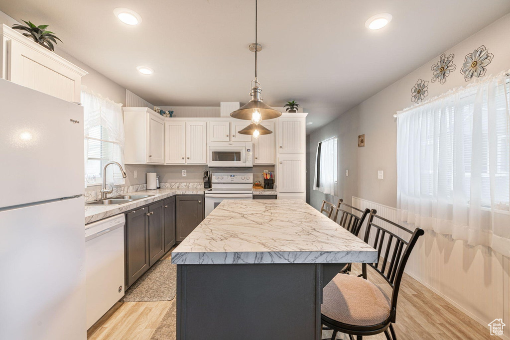 Kitchen featuring a center island, a sink, light countertops, white appliances, and white cabinetry