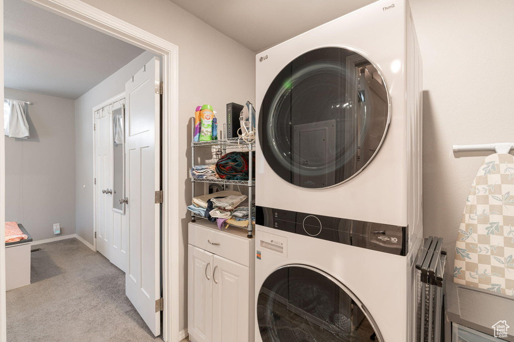 Laundry area featuring light carpet, stacked washer / drying machine, baseboards, and cabinet space