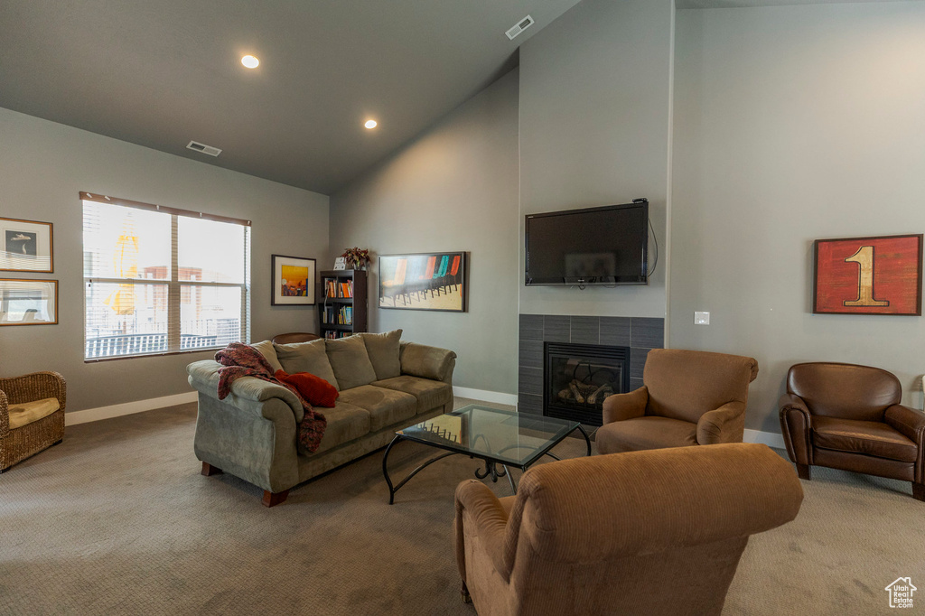 Living room with high vaulted ceiling, a tiled fireplace, carpet flooring, and visible vents