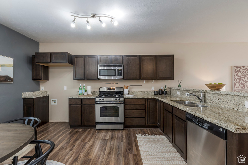 Kitchen featuring dark brown cabinetry, a peninsula, appliances with stainless steel finishes, dark wood-style flooring, and a sink