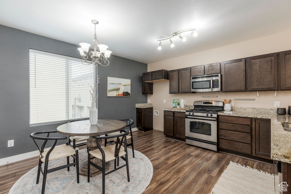 Kitchen with an inviting chandelier, dark wood-style flooring, dark brown cabinets, stainless steel appliances, and pendant lighting