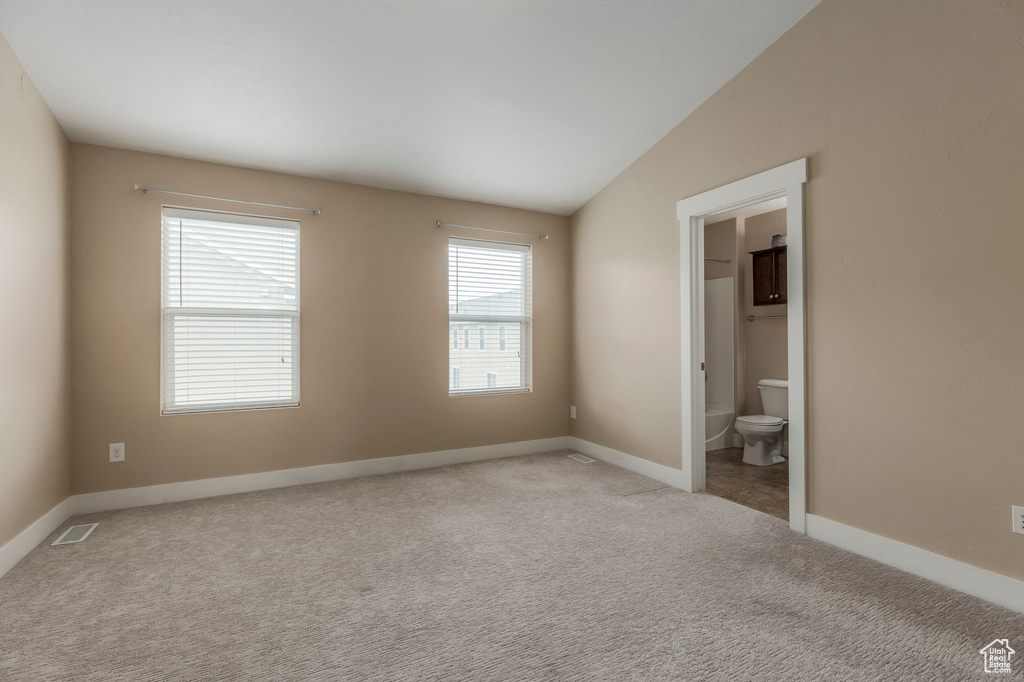 Unfurnished bedroom with visible vents, baseboards, ensuite bathroom, vaulted ceiling, and light carpet