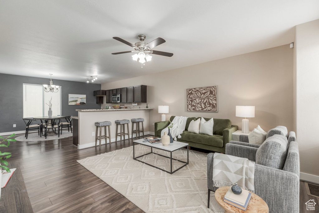Living room with dark wood-style floors, ceiling fan with notable chandelier, and baseboards