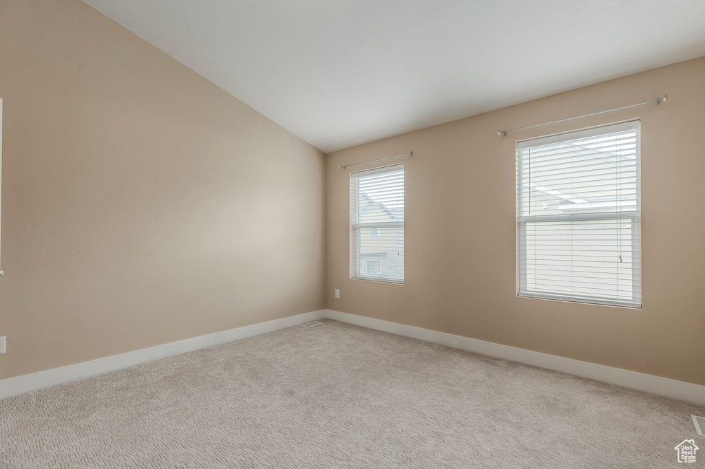 Carpeted spare room featuring baseboards and vaulted ceiling