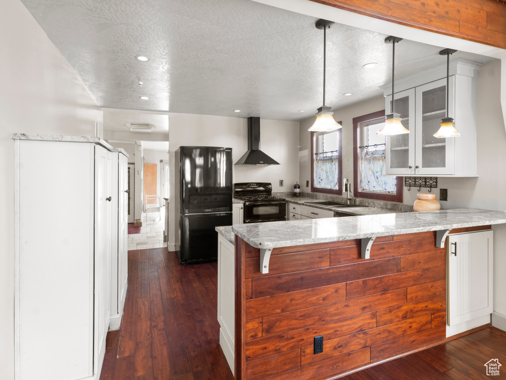Kitchen with wall chimney range hood, a peninsula, glass insert cabinets, black appliances, and a sink