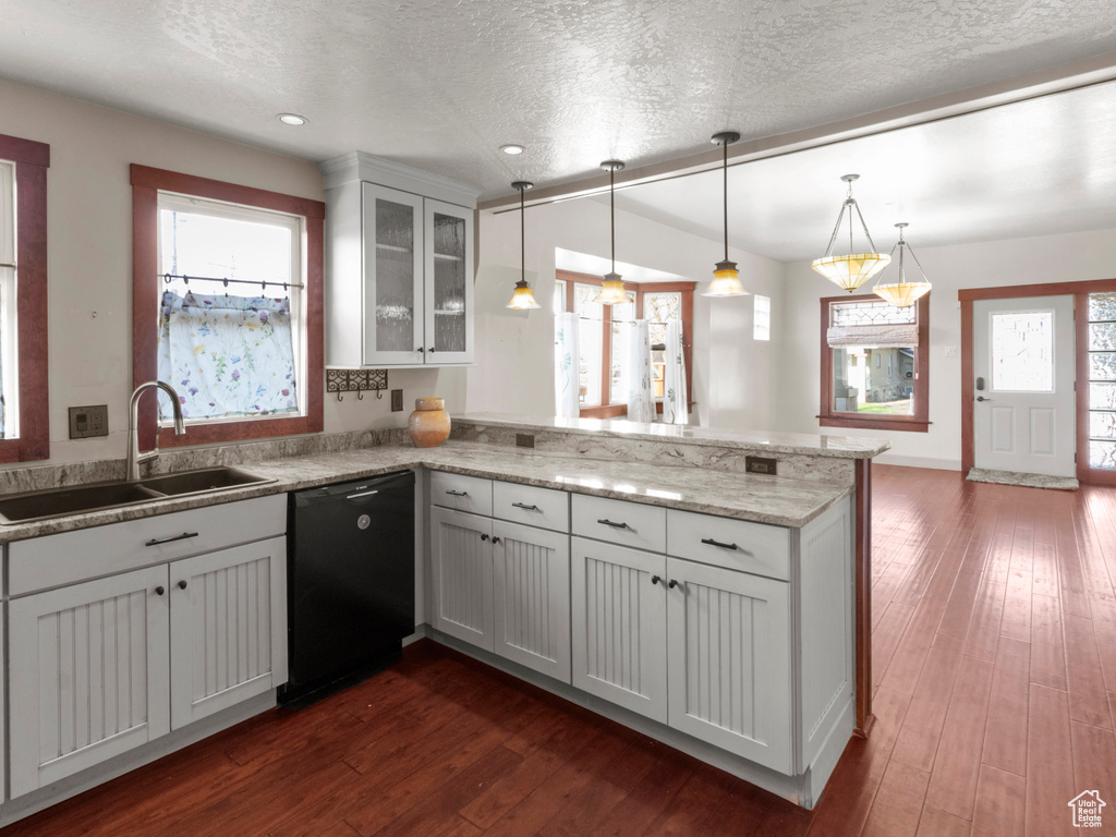 Kitchen with a peninsula, black dishwasher, dark wood-style flooring, a sink, and plenty of natural light