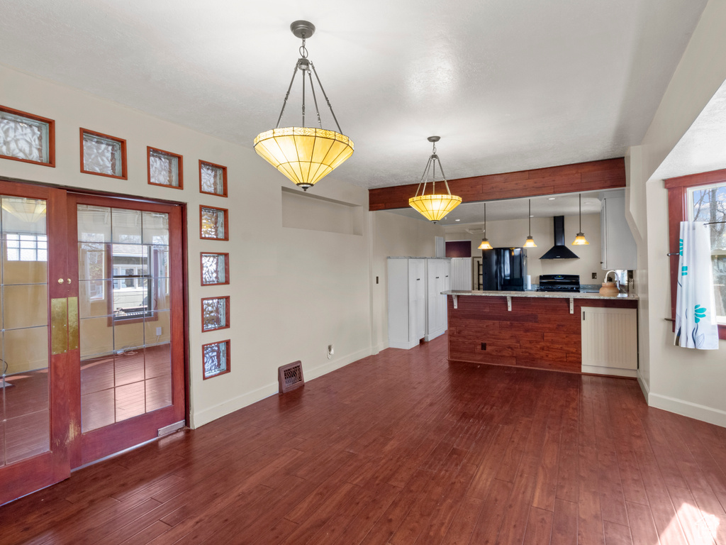 Kitchen featuring wall chimney range hood, a peninsula, dark wood-style flooring, and freestanding refrigerator