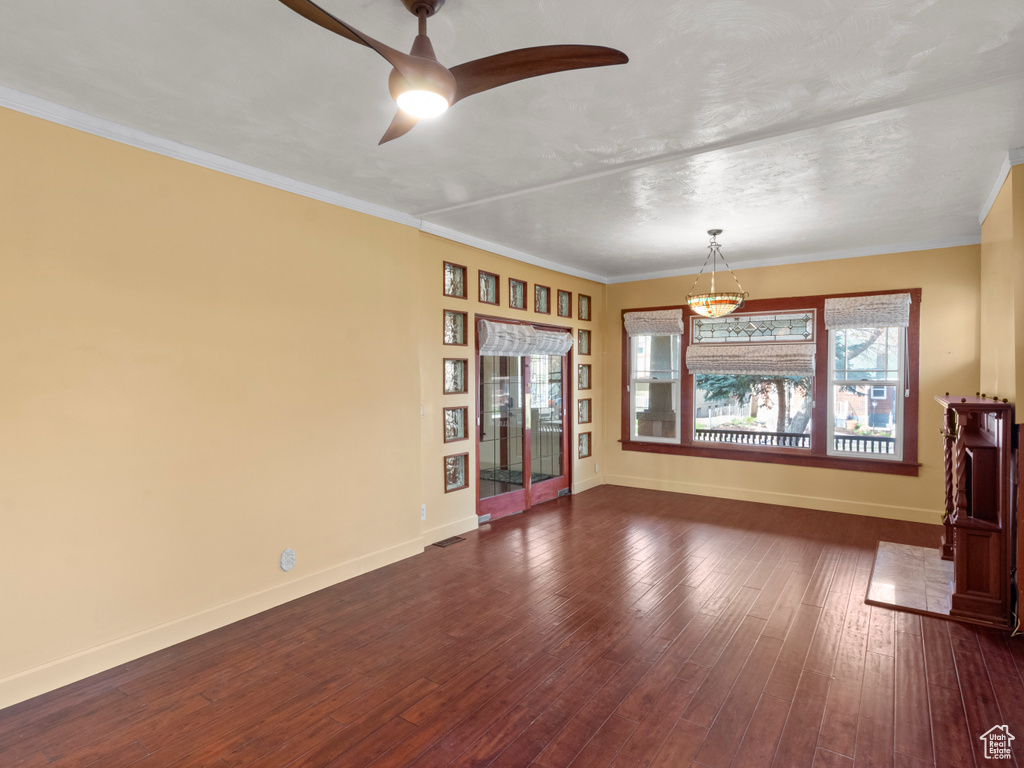 Spare room featuring dark wood-type flooring, baseboards, and ceiling fan with notable chandelier