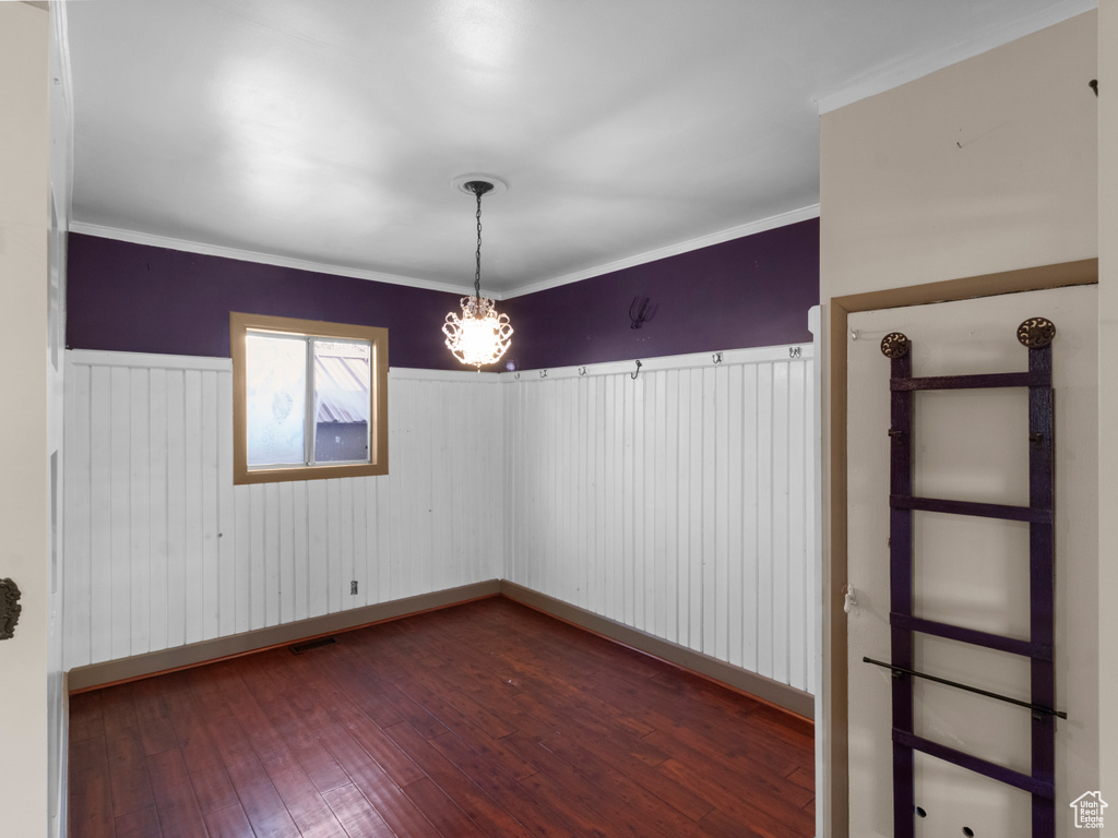 Spare room featuring an inviting chandelier, dark wood-type flooring, ornamental molding, visible vents, and a wainscoted wall