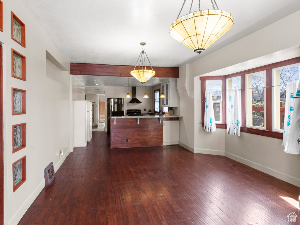 Interior space with glass insert cabinets, baseboards, wall chimney exhaust hood, a peninsula, and dark wood finished floors