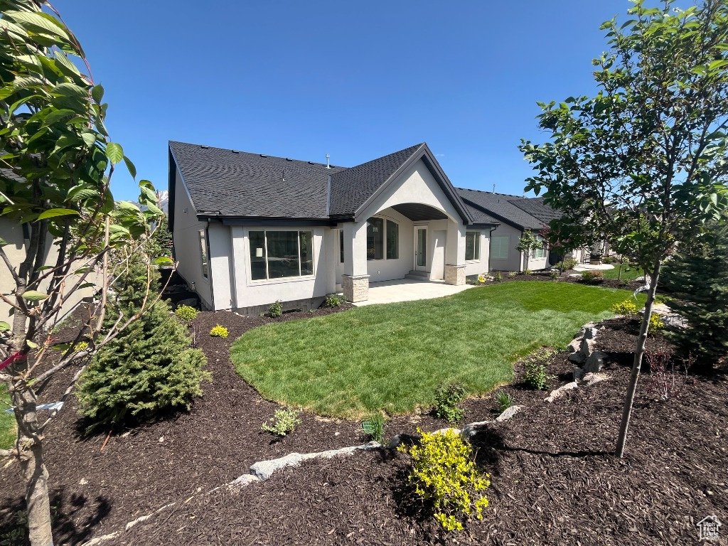 Rear view of property featuring roof with shingles, a patio, stucco siding, and a yard