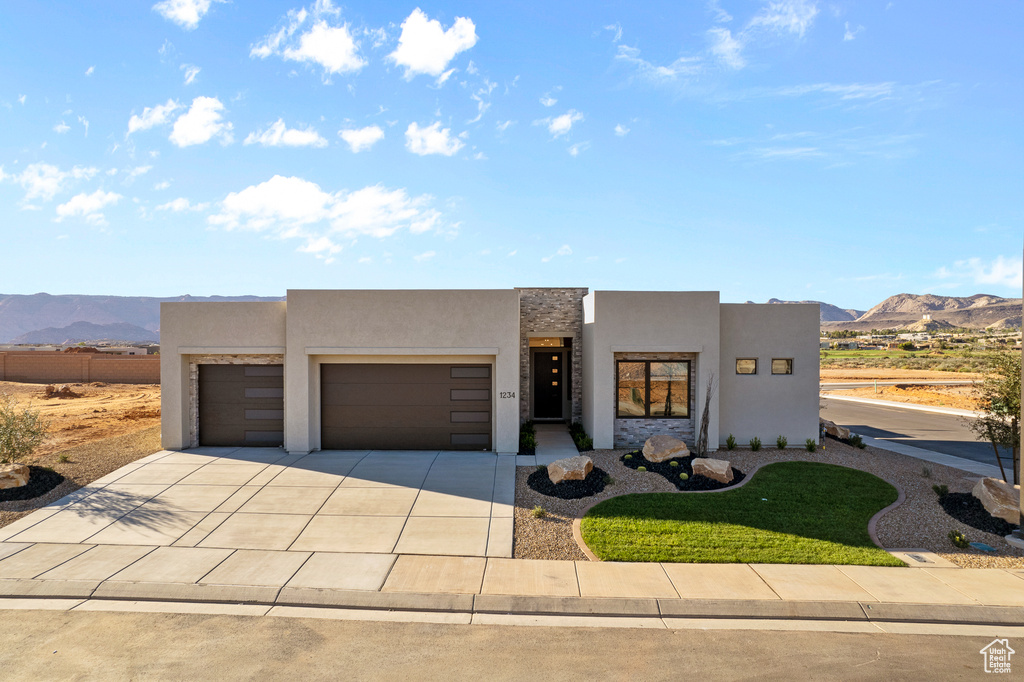Pueblo-style home with an attached garage, a mountain view, concrete driveway, and stucco siding