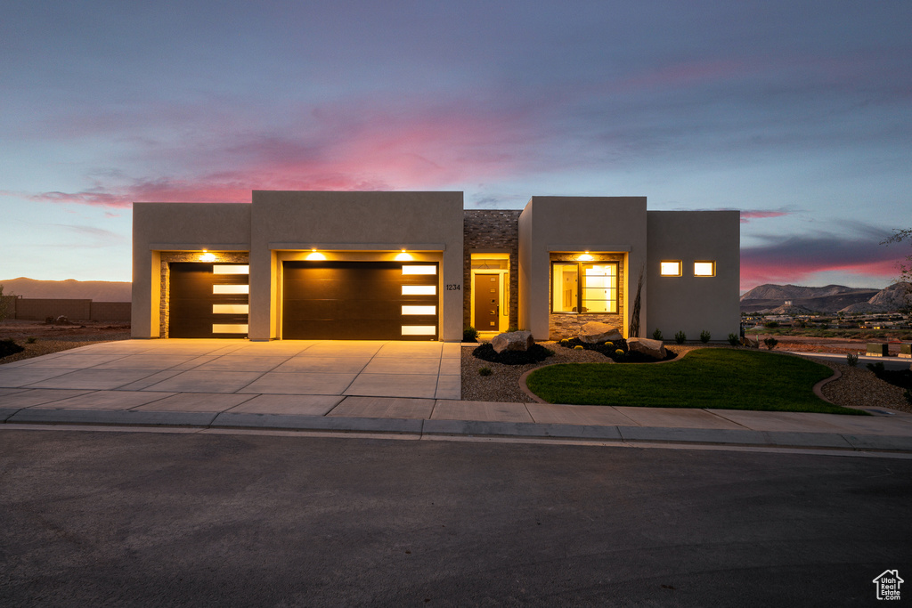 View of front of house featuring a garage, stucco siding, driveway, a lawn, and a mountain view