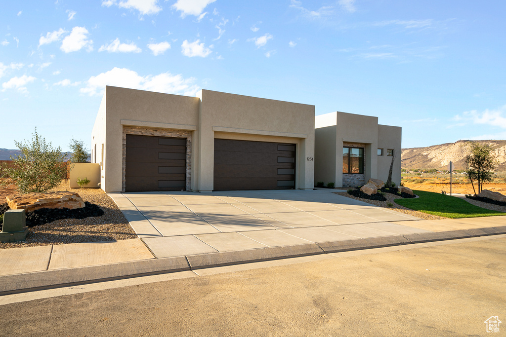 Pueblo-style home with stucco siding, a garage, concrete driveway, and a mountain view