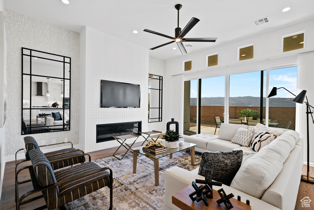 Living room with wood finished floors, ceiling fan, a large fireplace, recessed lighting, and baseboards