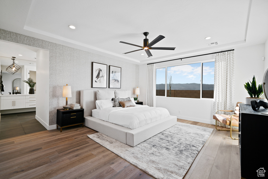 Bedroom with a raised ceiling, wood finished floors, recessed lighting, an accent wall, and baseboards
