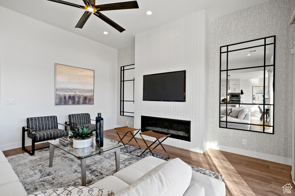Living area featuring baseboards, wood finished floors, ceiling fan, a large fireplace, and recessed lighting