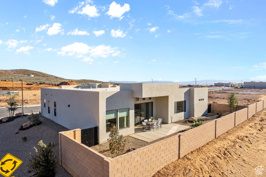 Back of house with stucco siding, a mountain view, a fenced backyard, and a patio area