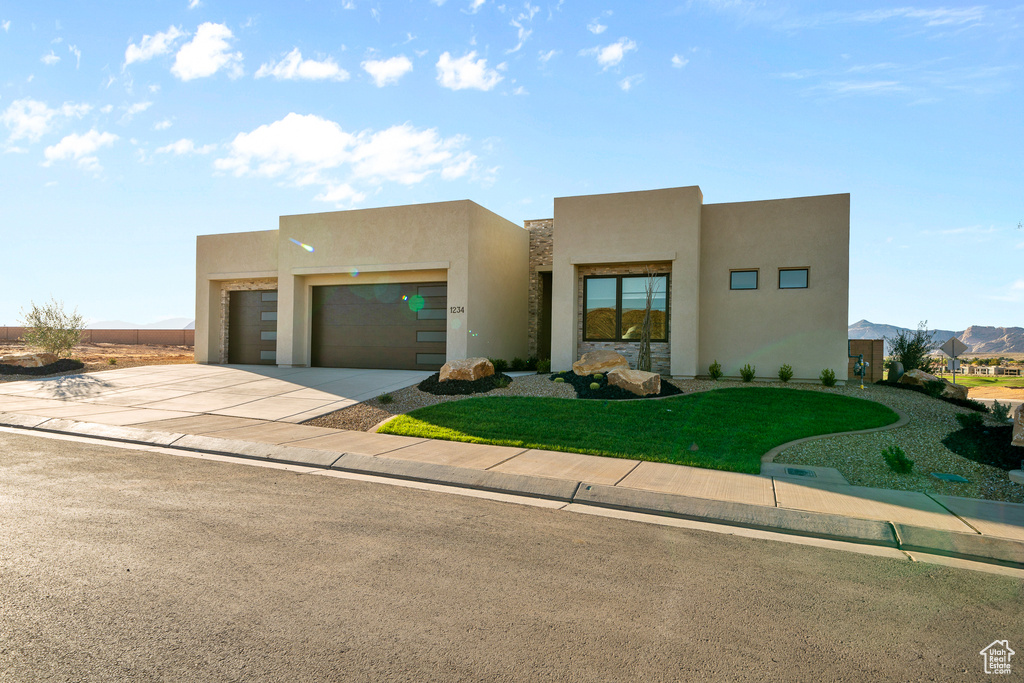 Pueblo-style house featuring an attached garage, stucco siding, driveway, and a front yard