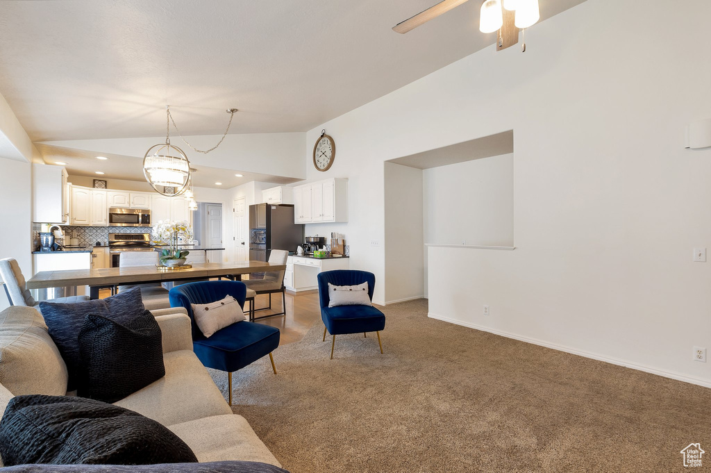 Living room featuring baseboards, recessed lighting, ceiling fan with notable chandelier, high vaulted ceiling, and light colored carpet