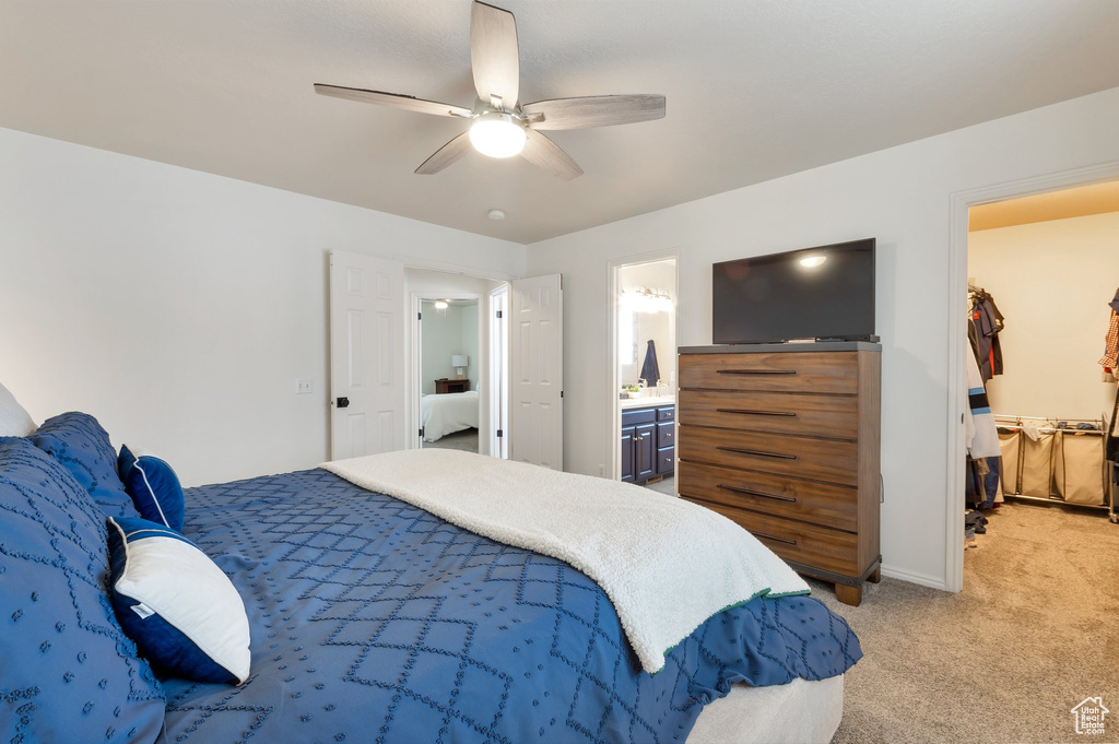 Bedroom featuring ensuite bathroom, ceiling fan, a spacious closet, light carpet, and baseboards