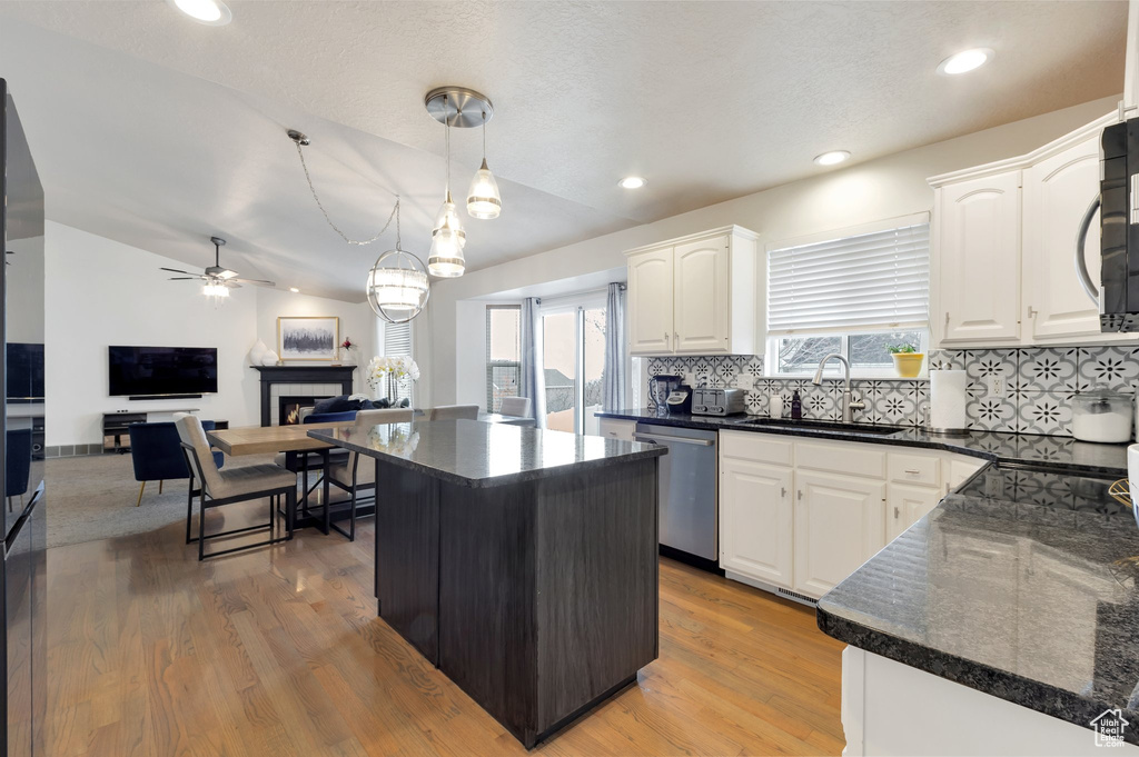 Kitchen featuring stainless steel dishwasher, white cabinetry, a ceiling fan, a tiled fireplace, and a sink
