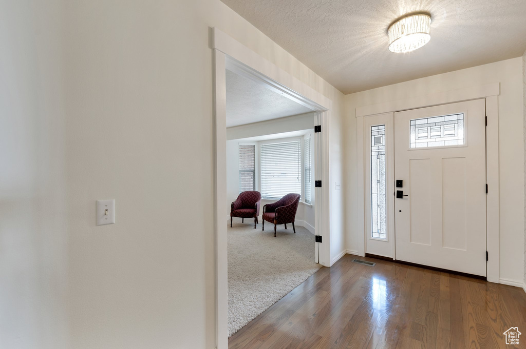 Foyer featuring baseboards, a textured ceiling, visible vents, carpet, and wood finished floors