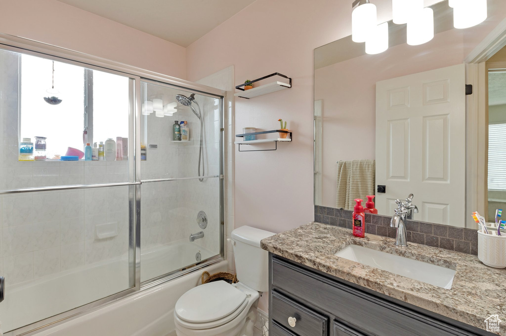 Full bath with shower / bath combination with glass door, vanity, and toilet