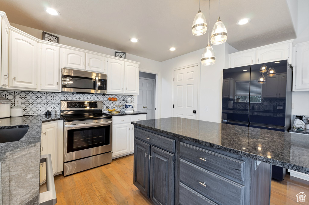 Kitchen featuring stainless steel appliances, dark stone countertops, white cabinets, and light wood-style flooring