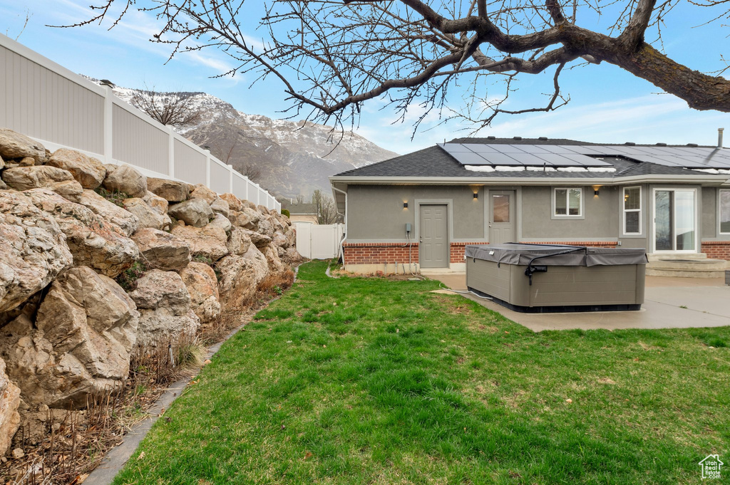 Back of property with roof mounted solar panels, a hot tub, a fenced backyard, a patio area, and brick siding