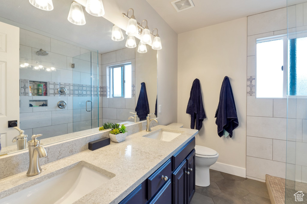 Full bath with toilet, tiled shower, a sink, and visible vents