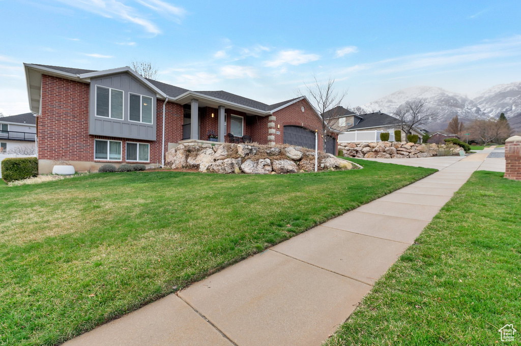 View of front of property with a mountain view, a garage, board and batten siding, brick siding, and a front lawn