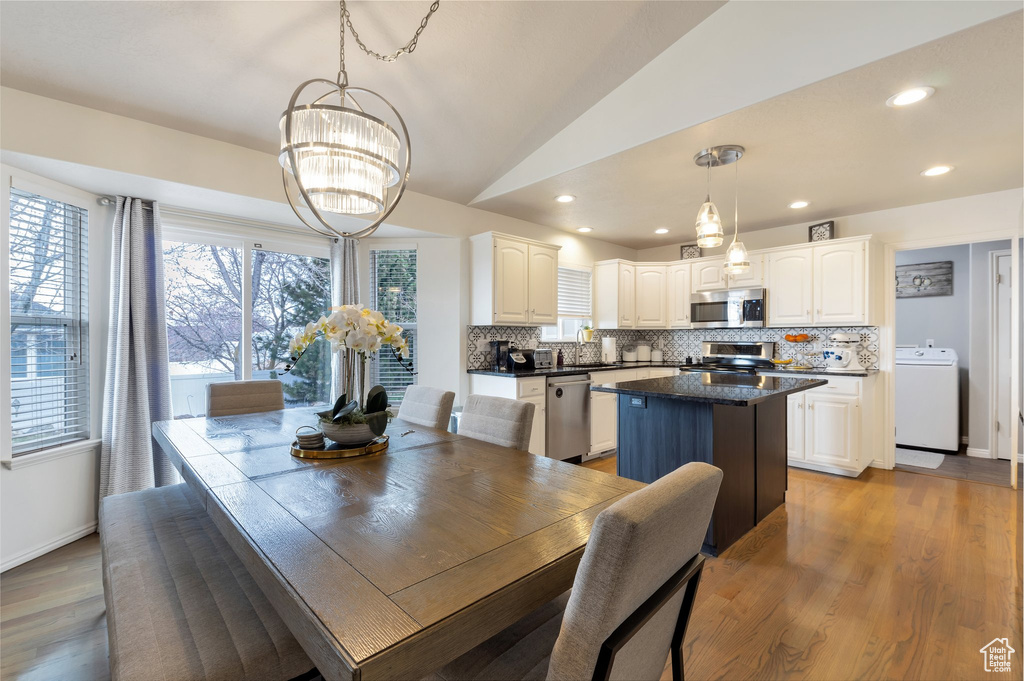 Dining room with washer / clothes dryer, light wood-style floors, a chandelier, and lofted ceiling