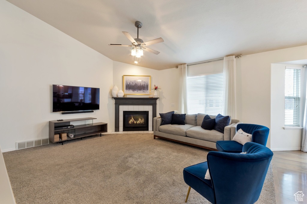 Living area with a ceiling fan, visible vents, lofted ceiling, a tile fireplace, and baseboards