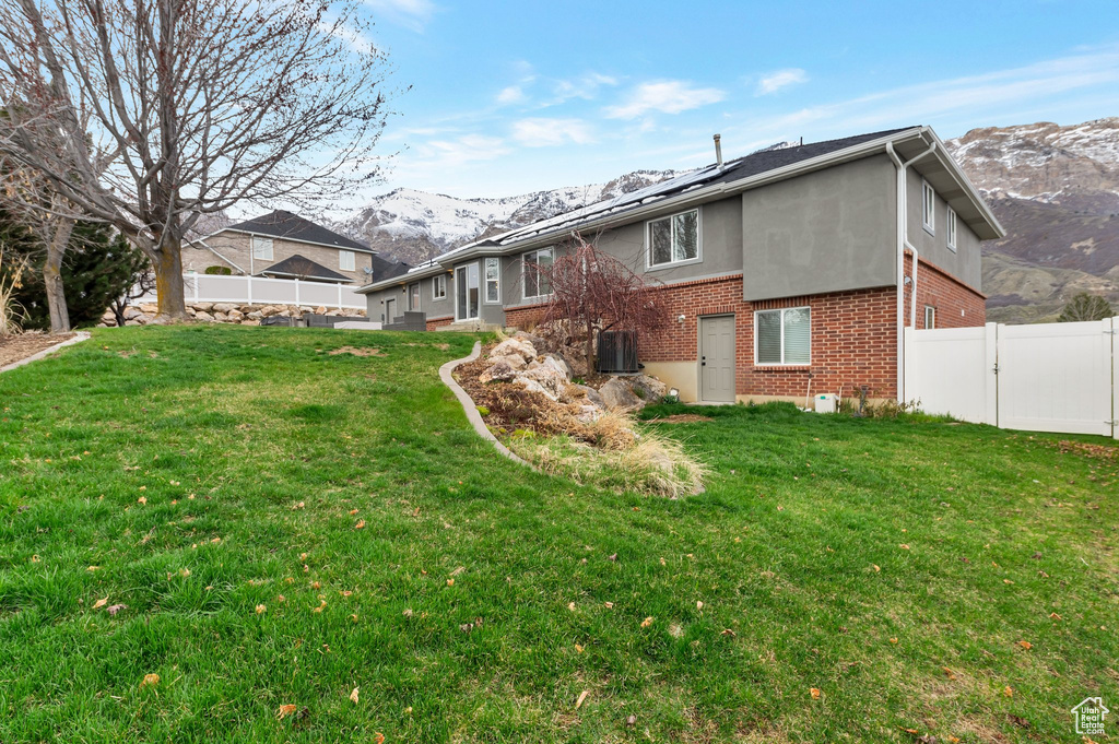 Back of property with fence, brick siding, a mountain view, and a lawn