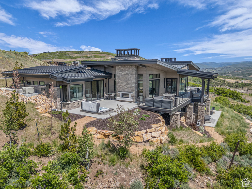 Back of property with stone siding, a standing seam roof, a mountain view, metal roof, and a patio area