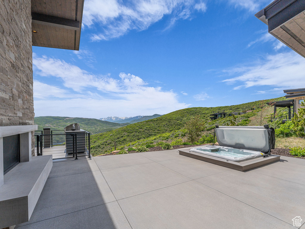 View of patio with a covered hot tub, a mountain view, an outdoor stone fireplace, and a grill
