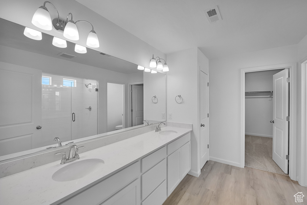 Bathroom with a shower stall, double vanity, a walk in closet, wood finished floors, and toilet